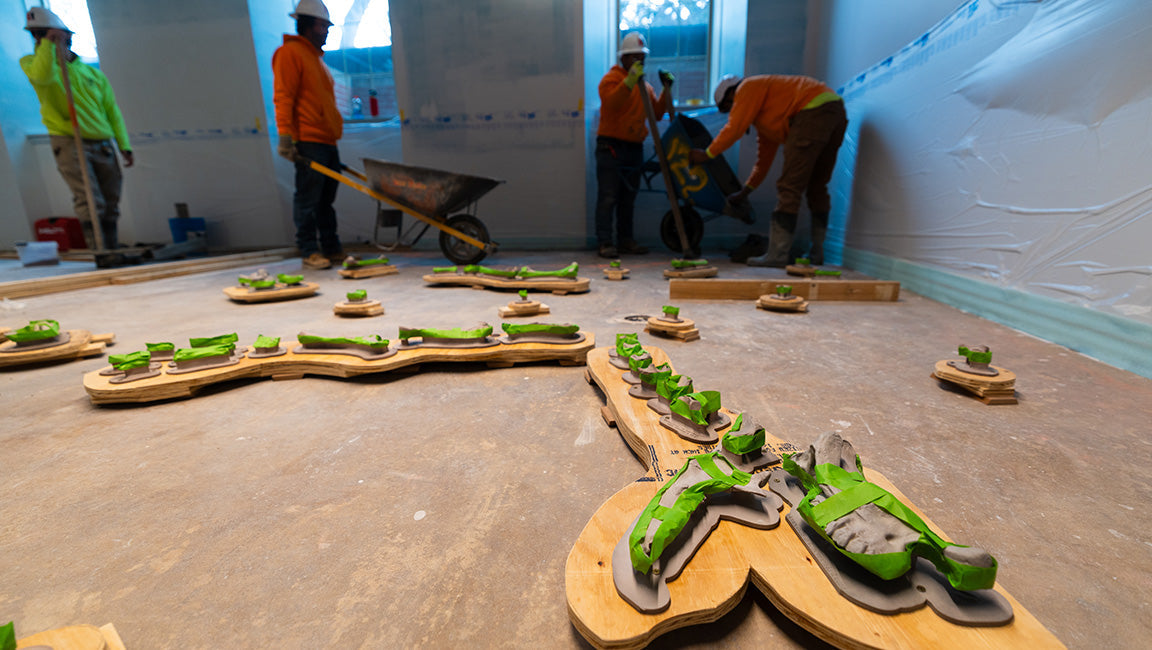 床に並ぶ3Dプリント化石骨と、奥でセメントを運ぶ作業員（米ネブラスカ大博物館 Morrill Hall 改修工事）